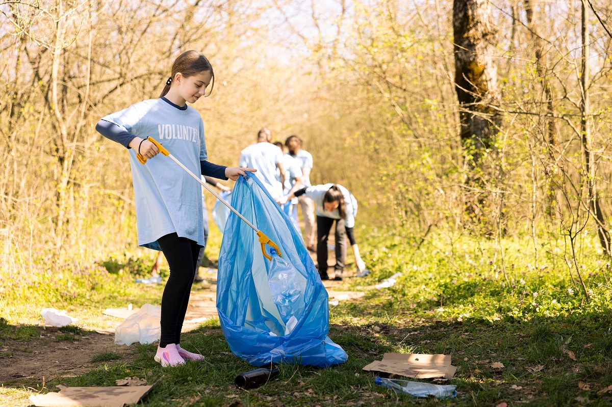 Fetița strânge gunoaie din pădure alături de alți voluntari