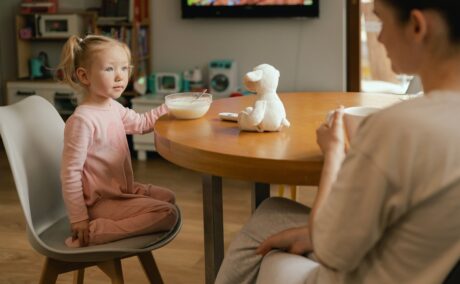 Mama își bea cafeaua în timp ce fiica ei își mănâncă micul dejun