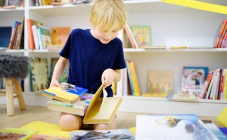 Băiat răsfoiește cărți în biblioteca de acasă