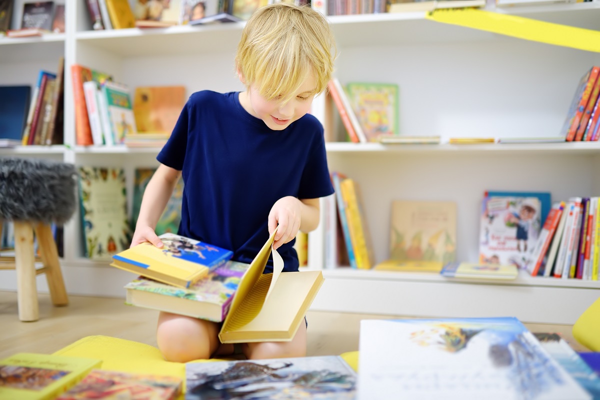 Băiat răsfoiește cărți în biblioteca de acasă