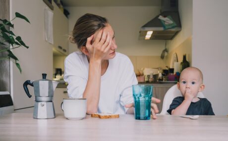 Mama epuizată stă la masă cu copilul care mănâncă