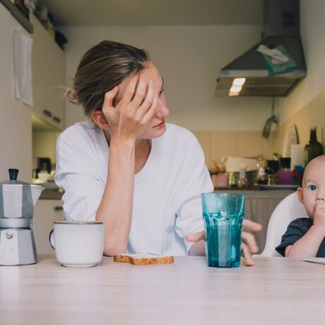Mama epuizată stă la masă cu copilul care mănâncă