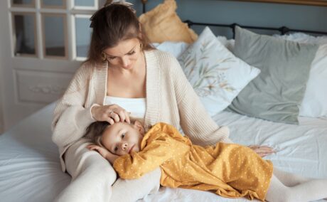 Mama își mângâie fetița pe păr în timp ce stau în pat și discută