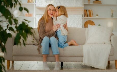 Fetița îi șoptește mamei care stă pe canapea ceva la ureche