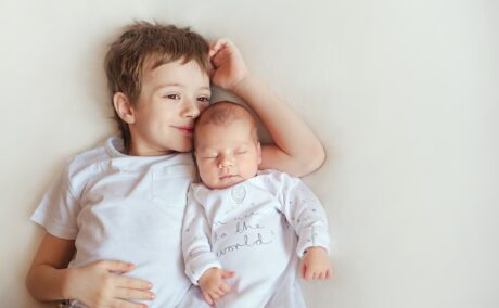 Fratele mai mare stă pe pat lângă fratele mai mic