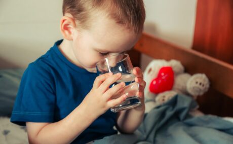 Băiat stă în pat și bea un pahar cu apă