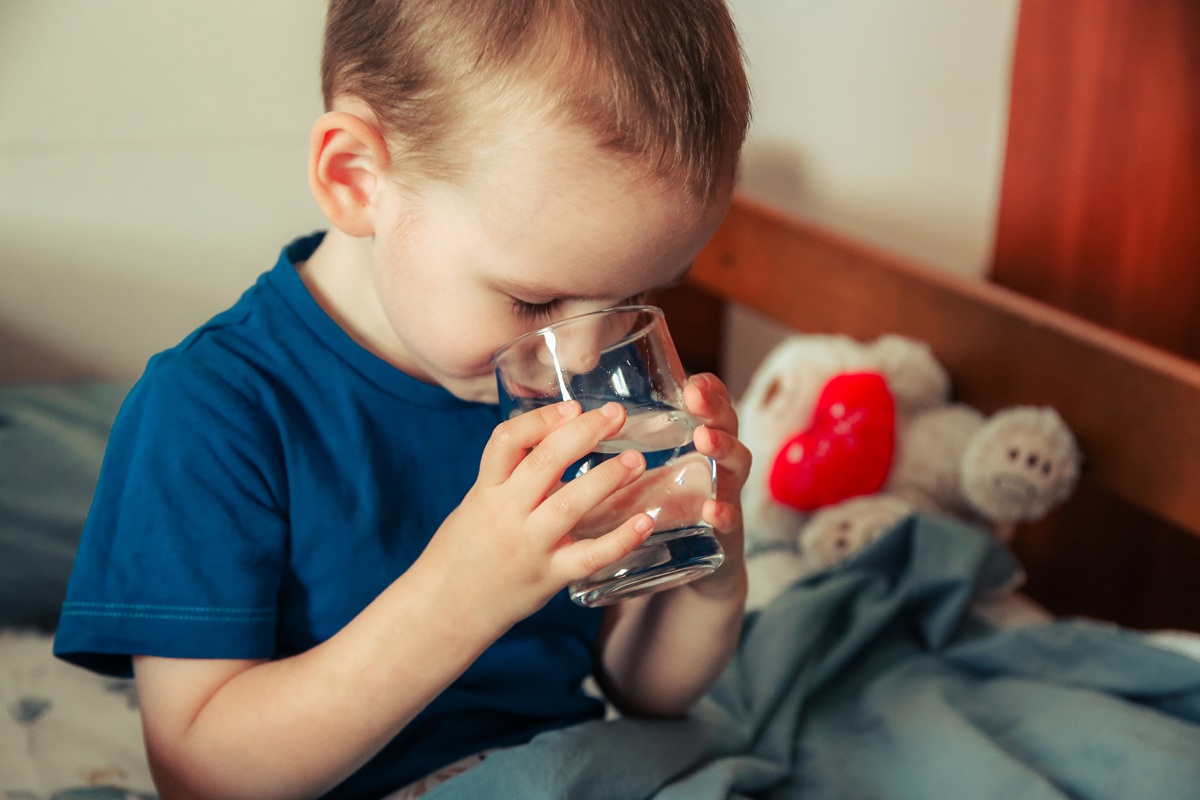 Băiat stă în pat și bea un pahar cu apă