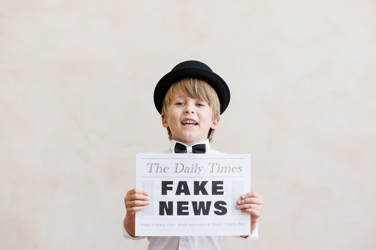 Băiat pozează cu o foaie pe care scrie fake news