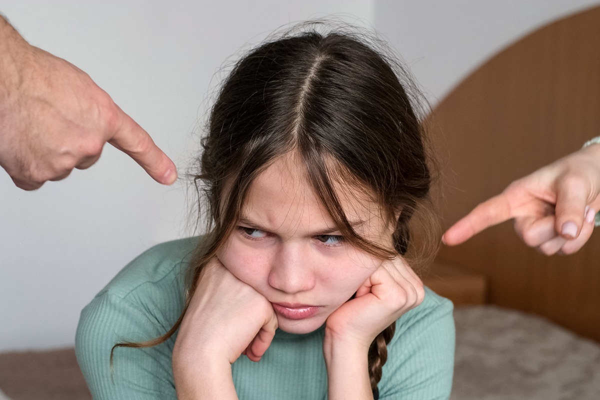 Fetiță stă supărată în timp ce este atenționată de mâinile părinților