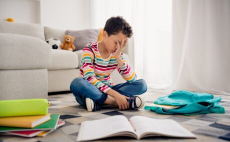 Băiat stă pe covor cu multe caiete și cărți în jurul lui