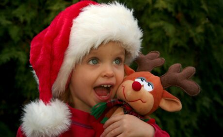 Fetiță costumată în Moș Crăciun ține un ren de pluș în brațe