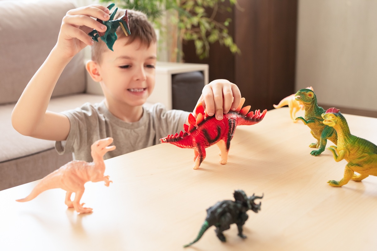 Băiat se joacă la masă cu câțiva dinozauri de jucărie