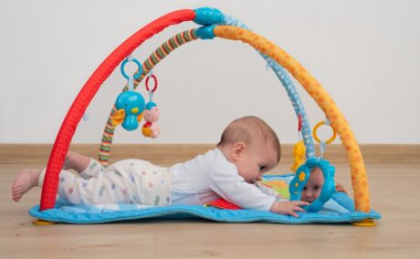 Bebeluș stă pe burtică pe salteluță și se uită în oglindă