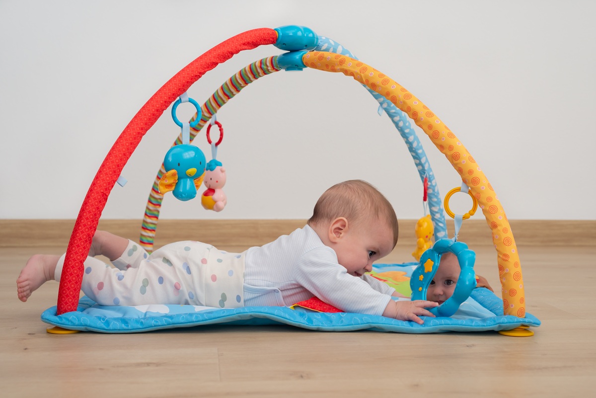 Bebeluș stă pe burtică pe salteluță și se uită în oglindă