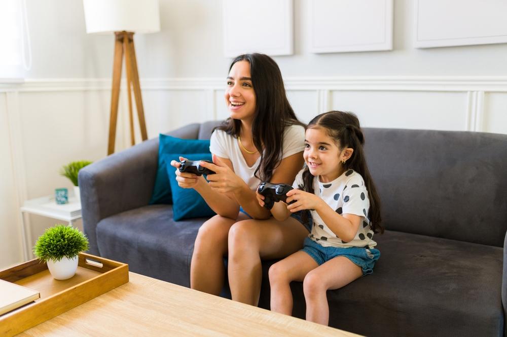 mama si fiica stand pe o canapea si jucandu-se un joc video