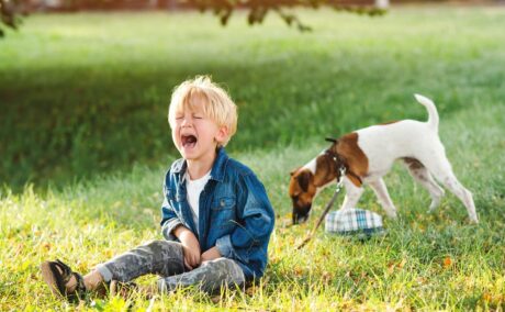 Un copil care sta pe iarba in parc langa un caine si plange